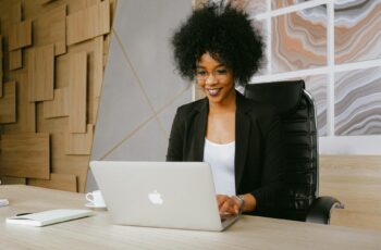 woman in black blazer sitting by the table while using macbook